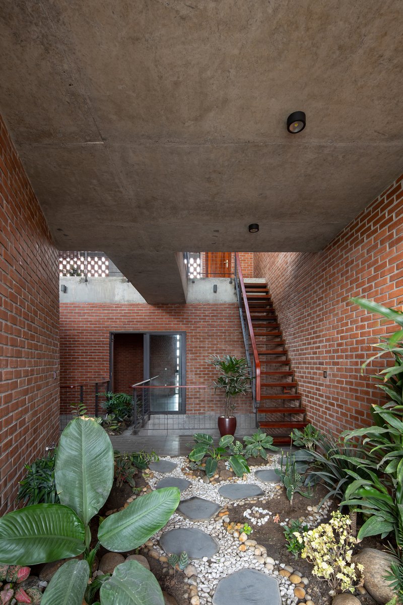 Ground-level courtyard with stepping stones, tropical plants, timber stair, and exposed concrete ceiling