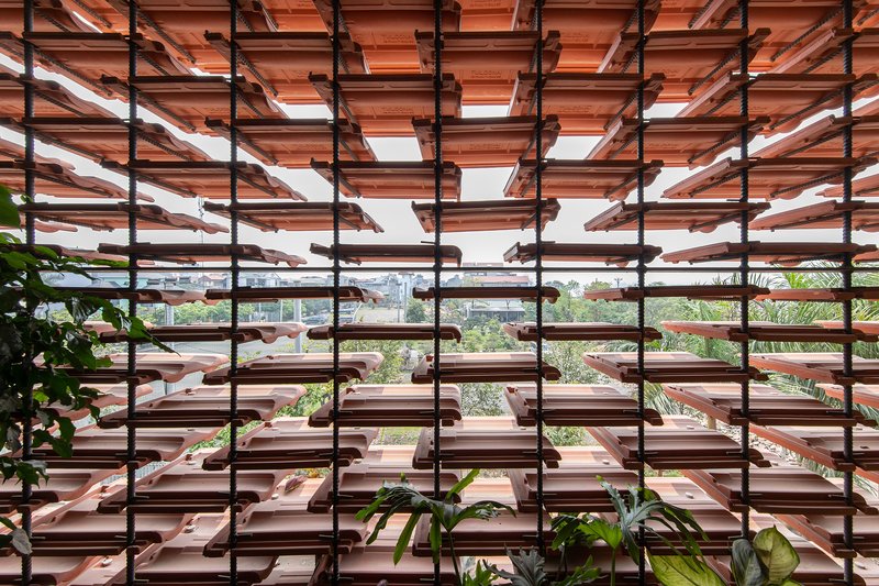 Clay tile brise-soleil screen with steel rod supports framing a view of rooftops and greenery