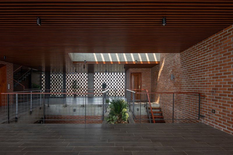 Perforated brick screen wall below a skylight casting striped shadows across the dark tile floor