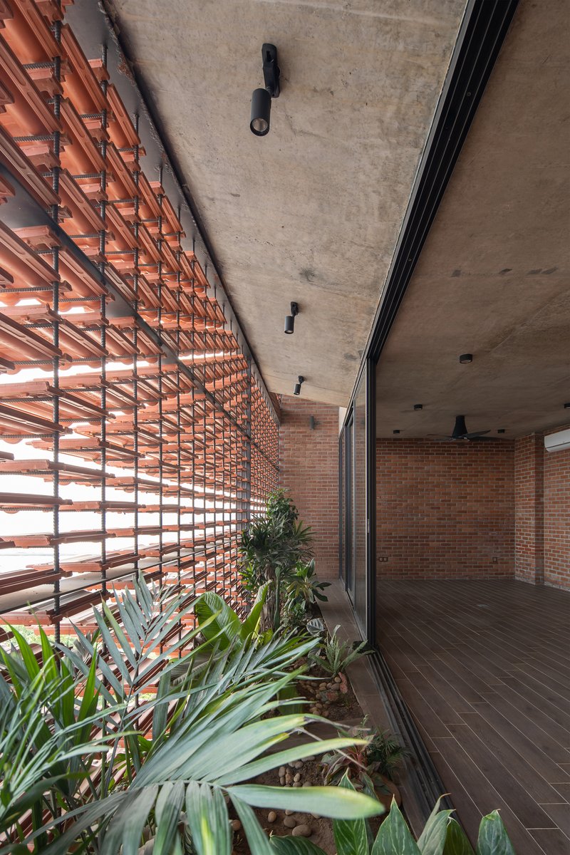 Covered terrace with horizontal terra-cotta louvers filtering daylight over a planted bed with succulents