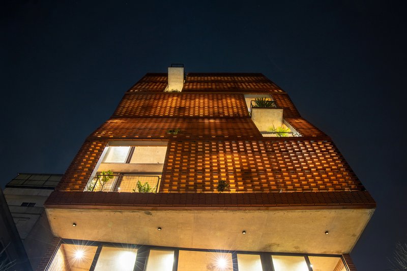 Upward view of the tapered brick facade with glazed openings at night under a dark blue sky