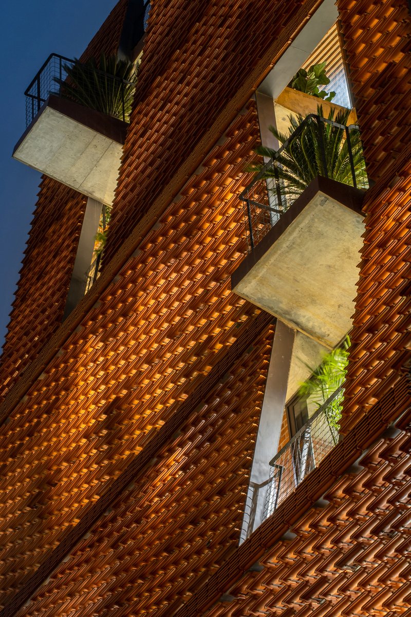 Staggered balconies with planted edges protruding through the openwork brick screen at twilight