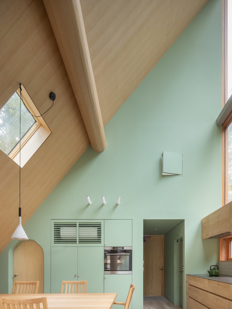 Vaulted plywood ceiling meeting a mint green wall with integrated cabinetry and angled skylight