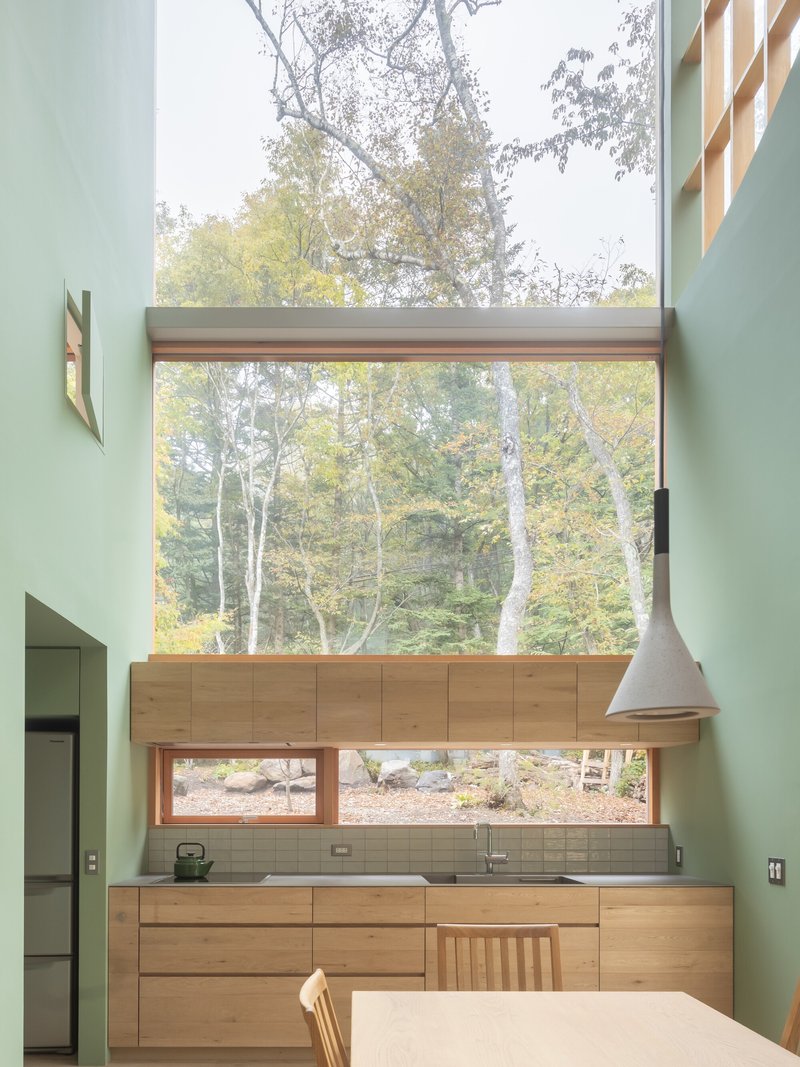 Kitchen with stacked windows framing birch trees and timber cabinetry beneath mint green walls