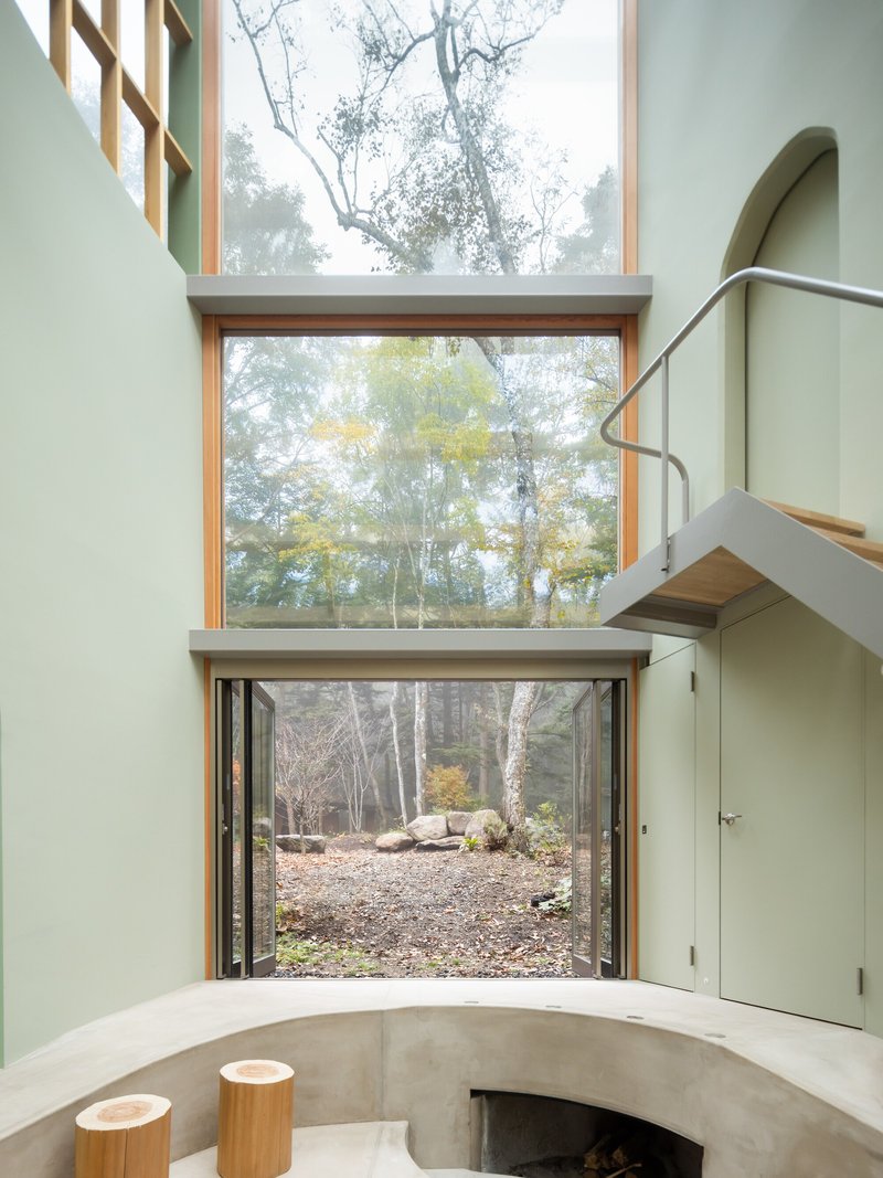 Stacked glazed openings framing autumn woodland with curved concrete bench and metal stair railing in foreground