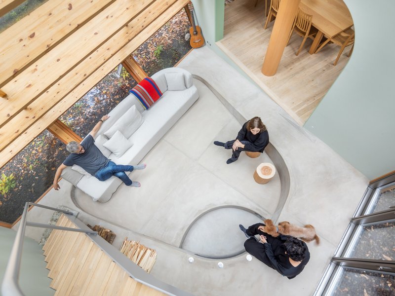 Top-down view of double-height living space with two people, a dog, and pale concrete floor