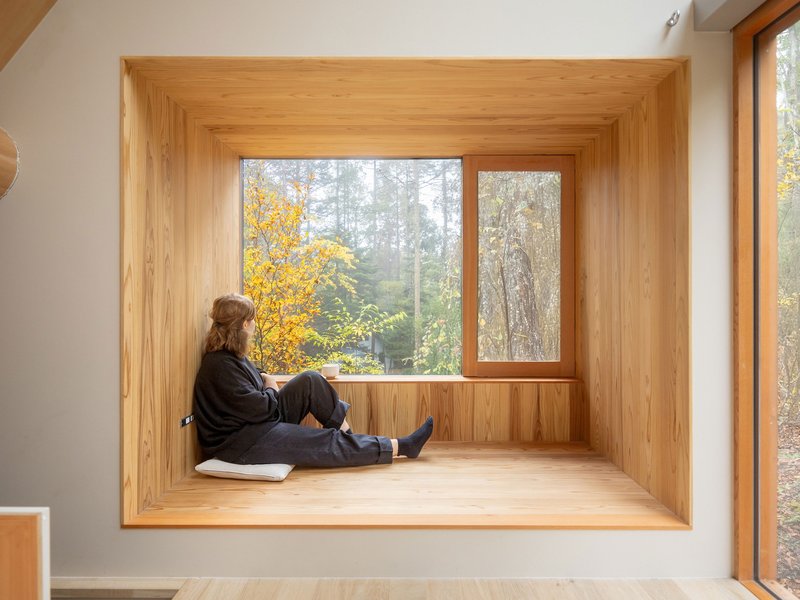 Deep timber-lined window seat with seated figure looking toward autumn trees outside
