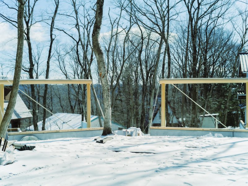 Snow-covered deck with timber railing frames looking into bare winter trees