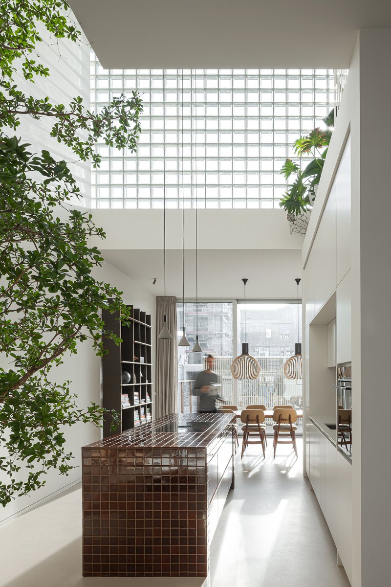 Double-height kitchen with dark tiled island and glass block skylight above a potted tree