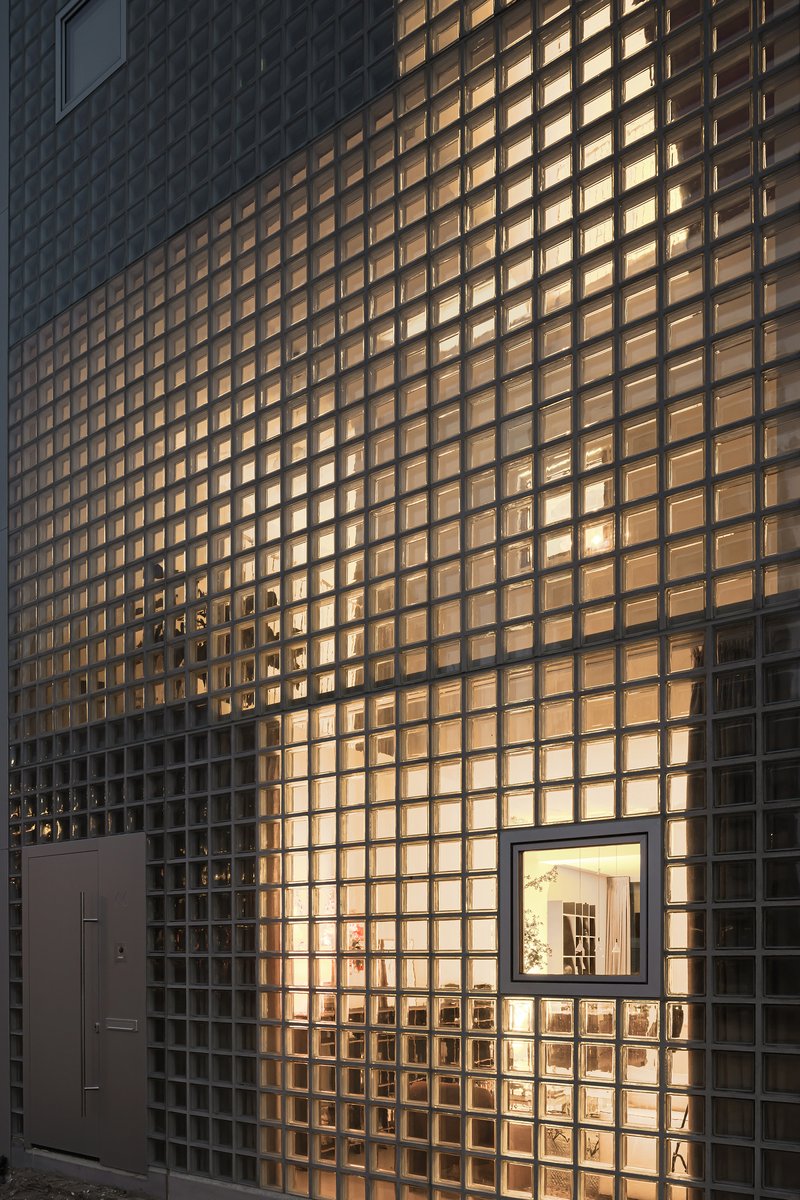 Glass block facade illuminated from within at dusk with a framed window opening