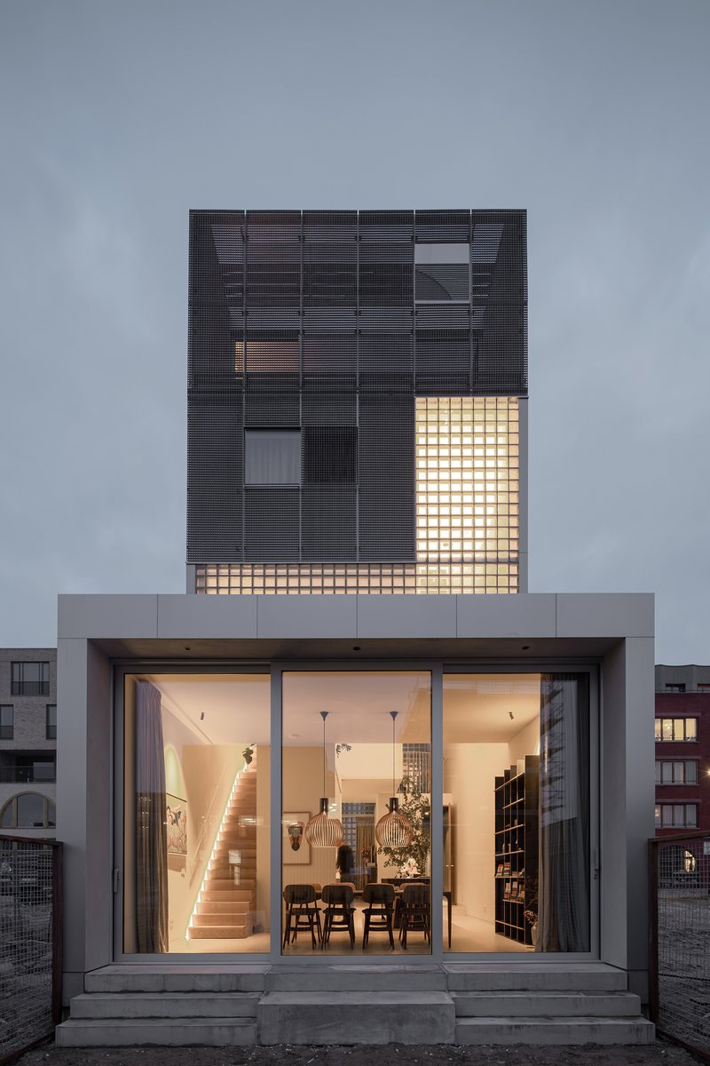Rear facade with concrete base and black glass brick upper level illuminated from within at twilight
