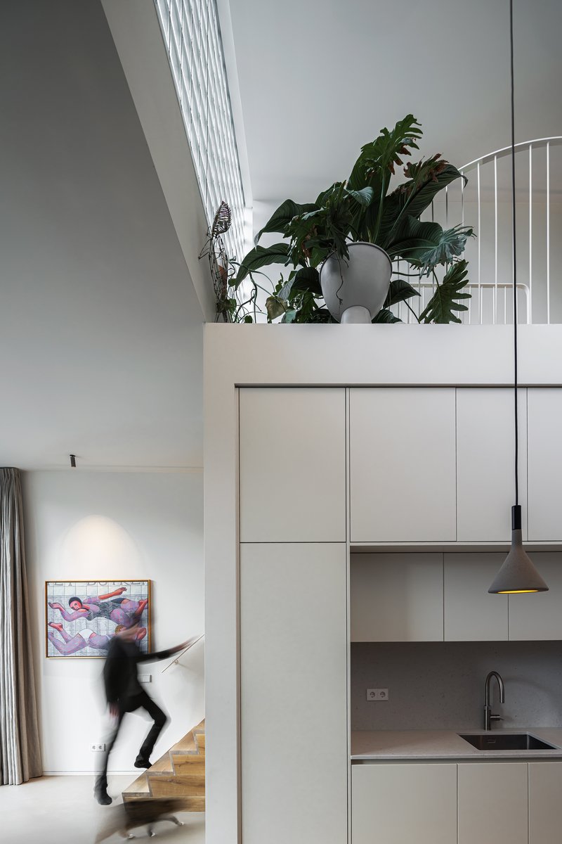 Kitchen cabinetry beneath upper level balcony with planted ledge and person descending timber stair