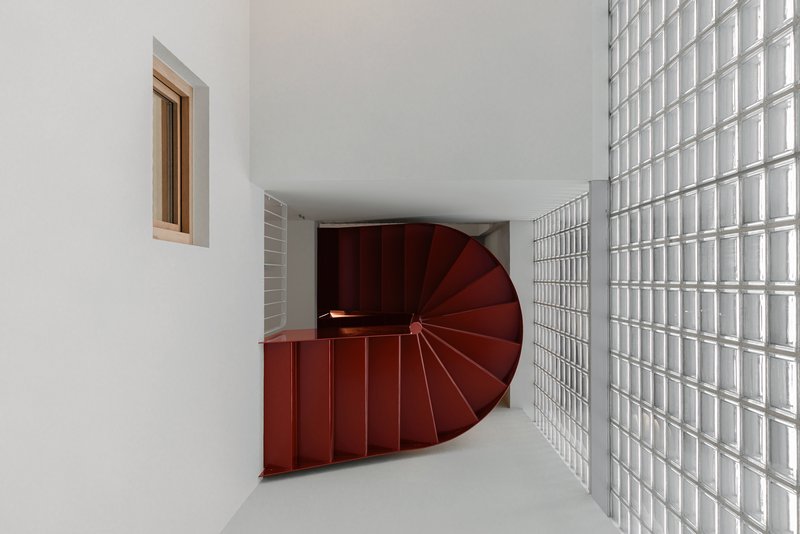 Top view of maroon spiral stair flanked by white glass block wall under curved soffit