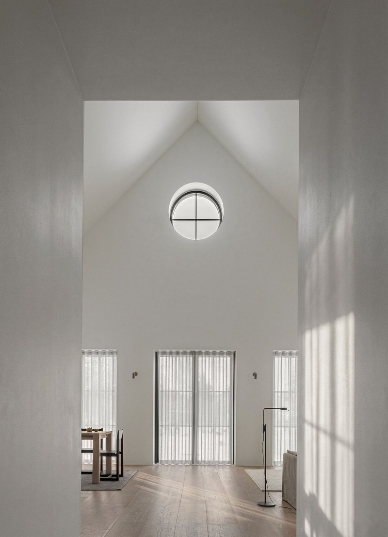 Double-height entry hall with vaulted ceiling, circular window, and fluted glass doors filtering afternoon light