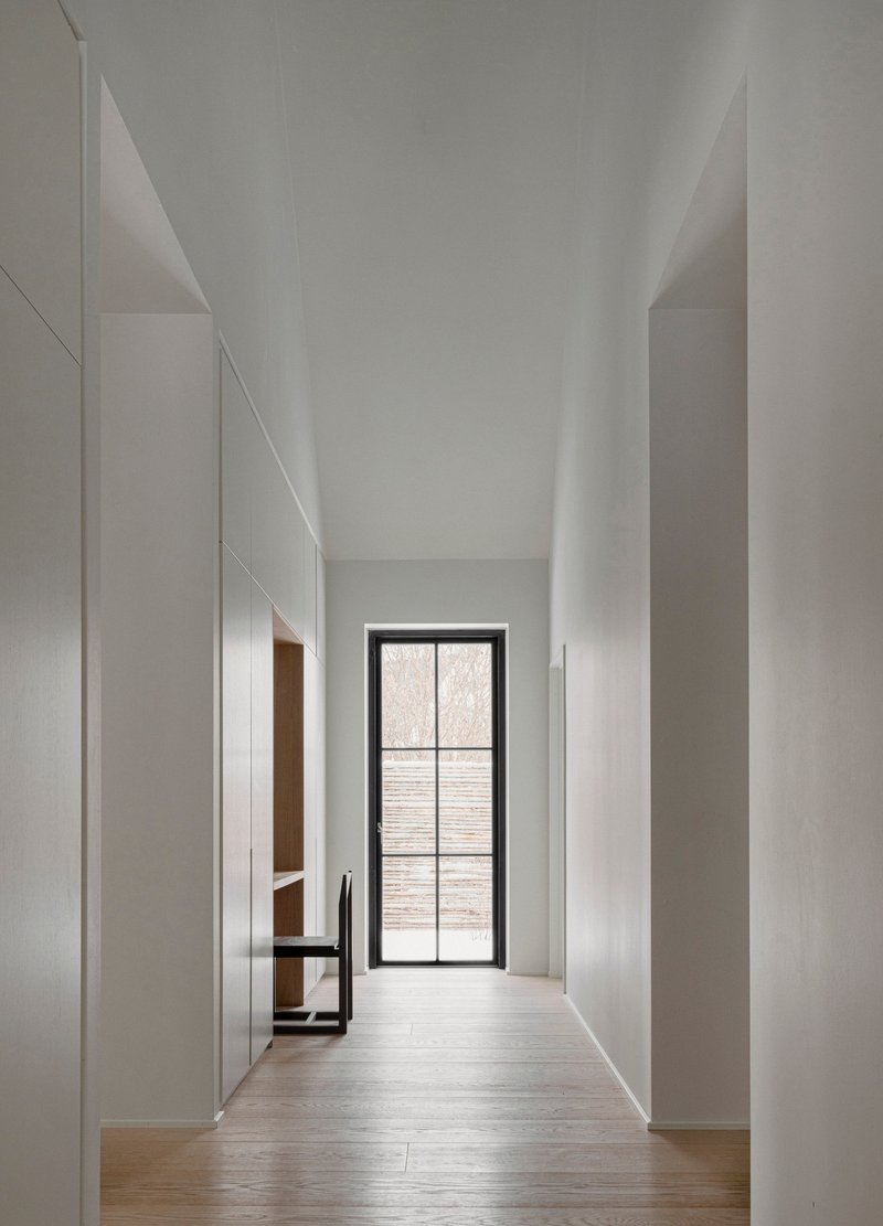 Narrow corridor with flush white cabinetry leading to a steel-framed glass door at the end
