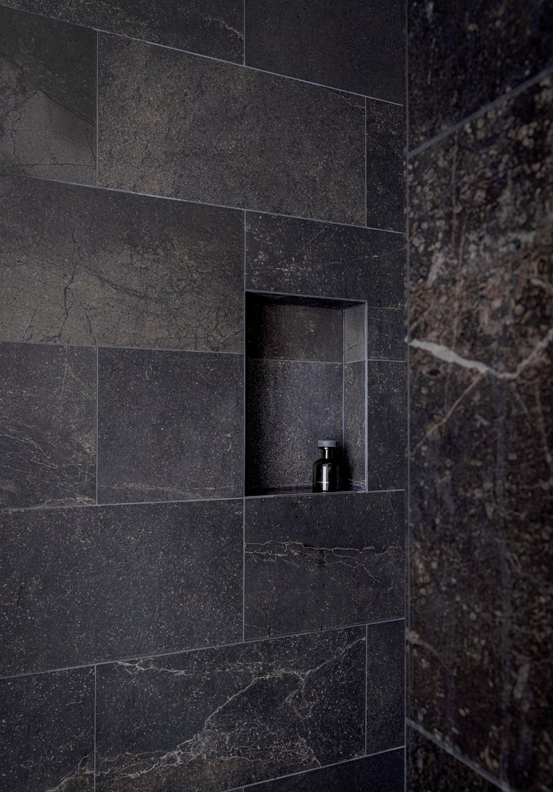 Recessed shower niche in dark grey stone tile wall with a single dispenser bottle
