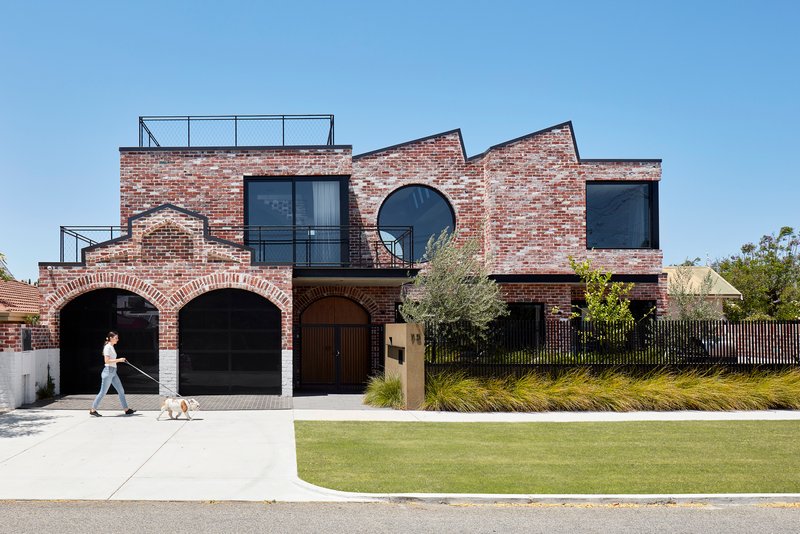 Street view of the red brick facade with arched openings and a person walking a dog