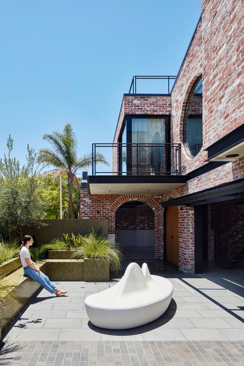 Courtyard with white sculptural seating and a woman sitting on the concrete planter edge