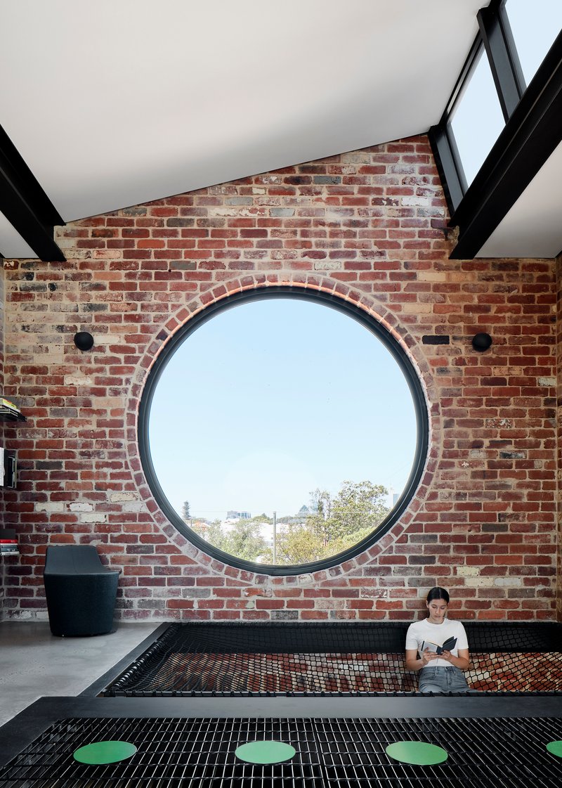 Circular window framed in exposed brick wall with a seated figure on a suspended mesh platform