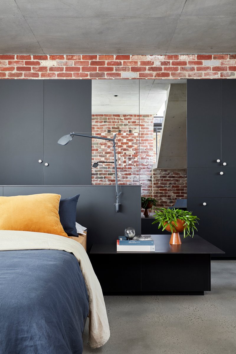 Bedroom with black built-in cabinetry and exposed brick wall visible through doorway opening