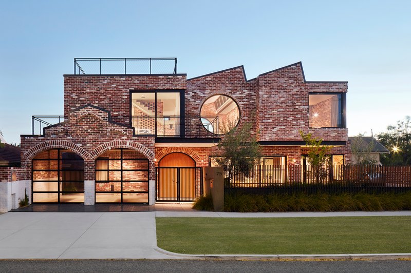 Street facade with brick arches framing garage doors and a circular window at dusk