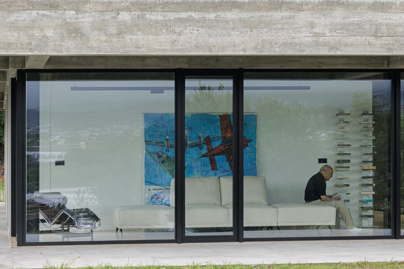 Exterior view of floor-to-ceiling glazing with a person seated inside beneath board-formed concrete overhang
