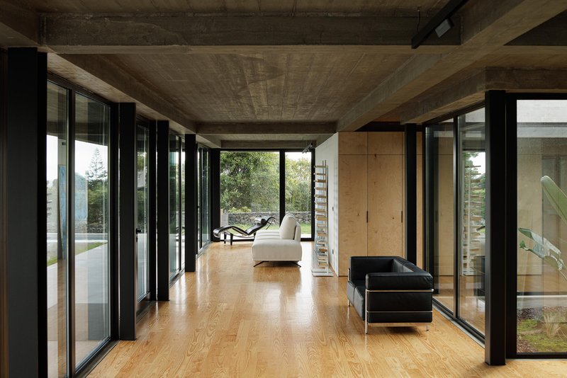 Interior corridor with light wood flooring and black steel columns framing views to the garden