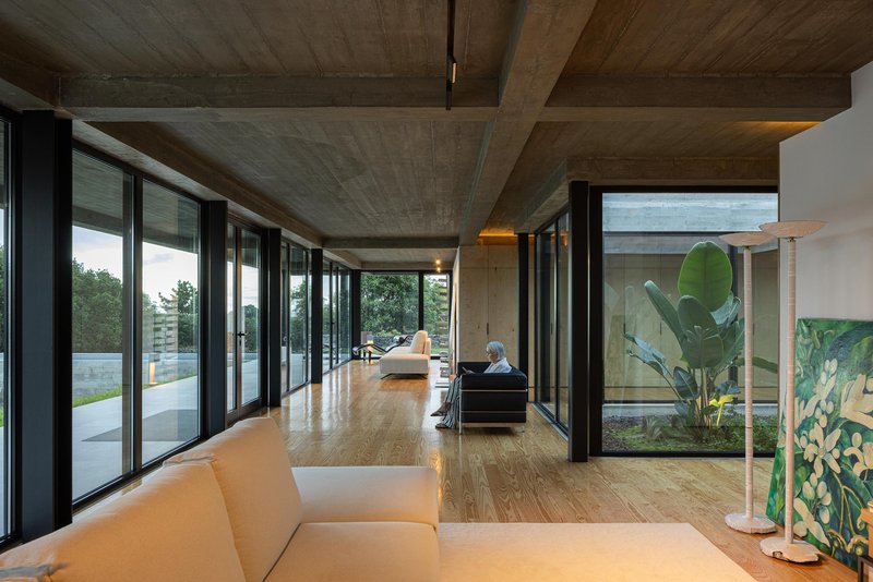 Long interior view through the glazed corridor showing banana leaf plant in courtyard beyond