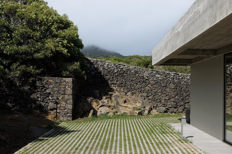 Courtyard with grid-patterned paving and volcanic stone walls against a mist-covered hillside