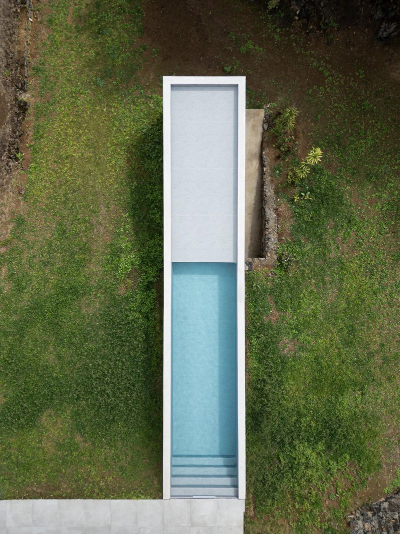 Aerial view of a narrow lap pool with submerged steps surrounded by grass and weathered stone