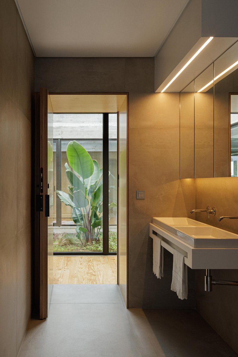 Bathroom vanity with concrete floor and view through glass door to courtyard with tropical plants
