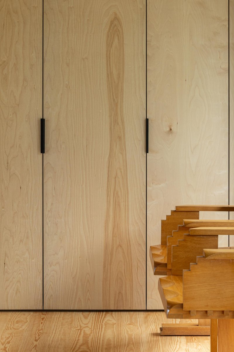 Detail of light plywood panels with black finger pulls beside sculptural timber step element
