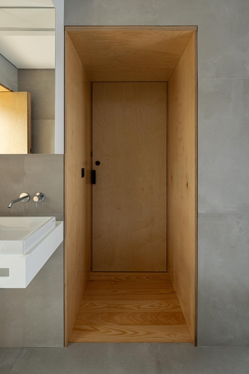 Timber-lined door niche set within polished concrete walls adjacent to bathroom vanity