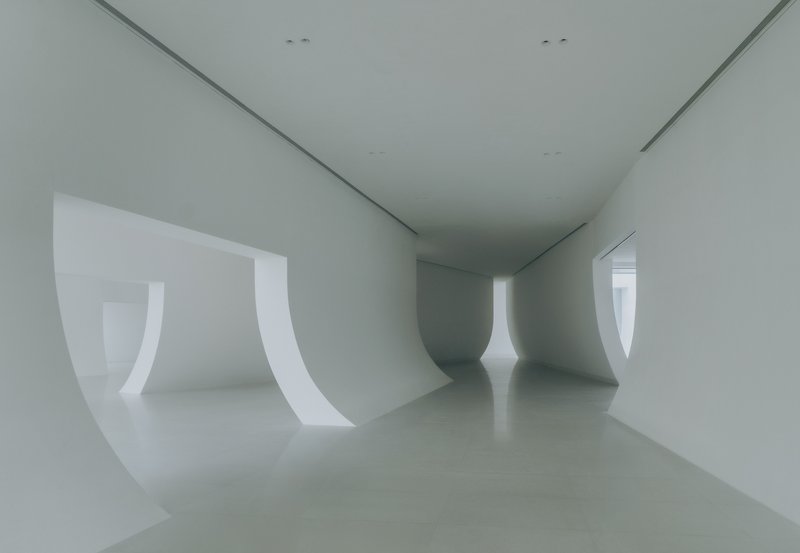 Interior gallery with curved white walls and window openings creating continuous spatial flow