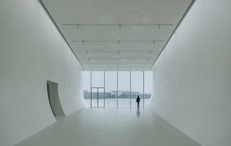 Gallery space with curved white walls and full-height glazing overlooking a misty waterfront