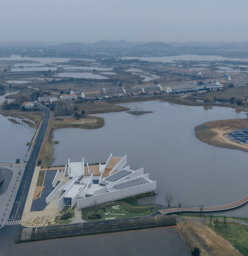 Aerial view of the white multi-winged complex alongside a river and wetlands under hazy sky