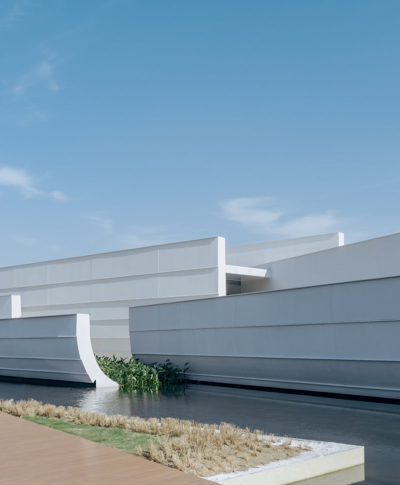 White horizontal panel facade with curved relief adjacent to a water feature and planted grasses