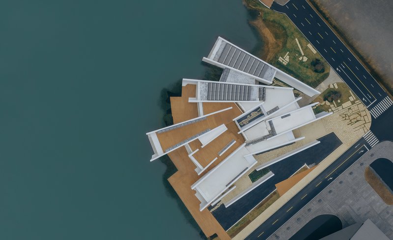 Aerial view of white angular volumes with timber decking extending over teal water
