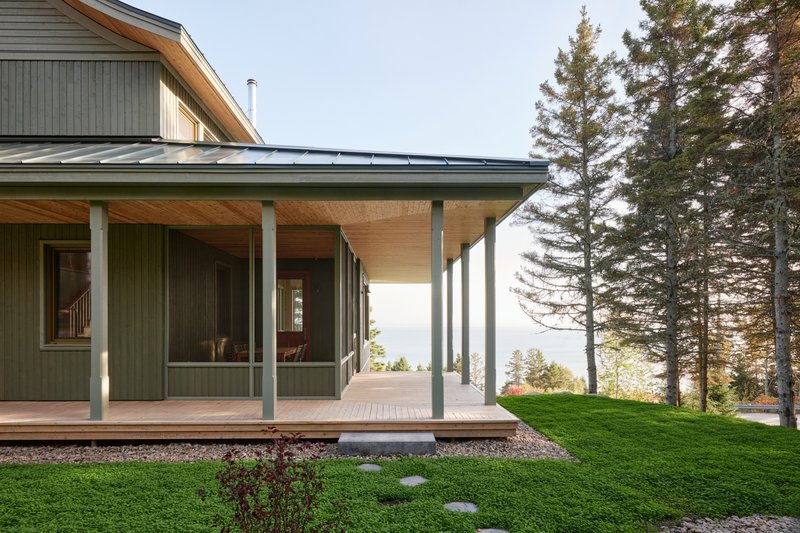 Covered porch with slim steel columns and plywood ceiling overlooking a lawn and distant treeline