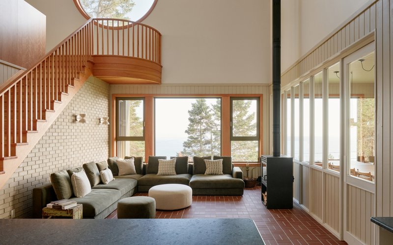 Double-height living room with curved wood stair balustrade and white brick fireplace wall beneath skylight