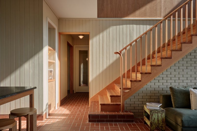 Entry hall with timber staircase, terracotta tile floor and white panelled walls in afternoon light