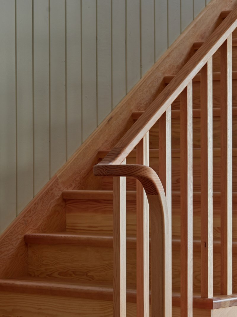 Detail of timber staircase with curved handrail and vertical balustrade against painted panelled wall