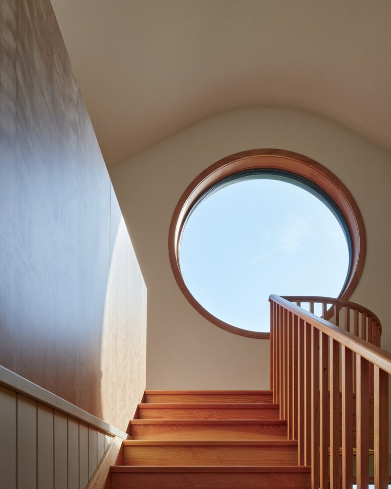 Upper staircase landing with large circular window framed in timber under a vaulted ceiling