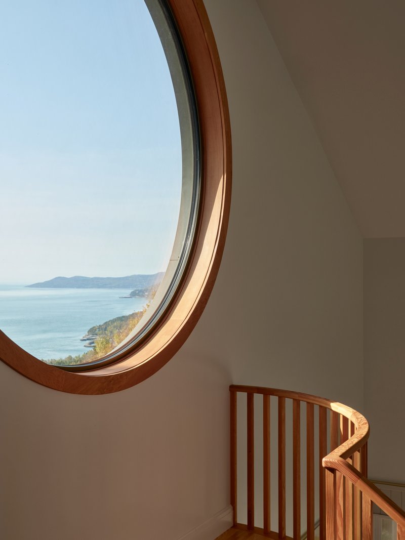 Circular window overlooking coastal landscape with curved timber railing catching morning sunlight