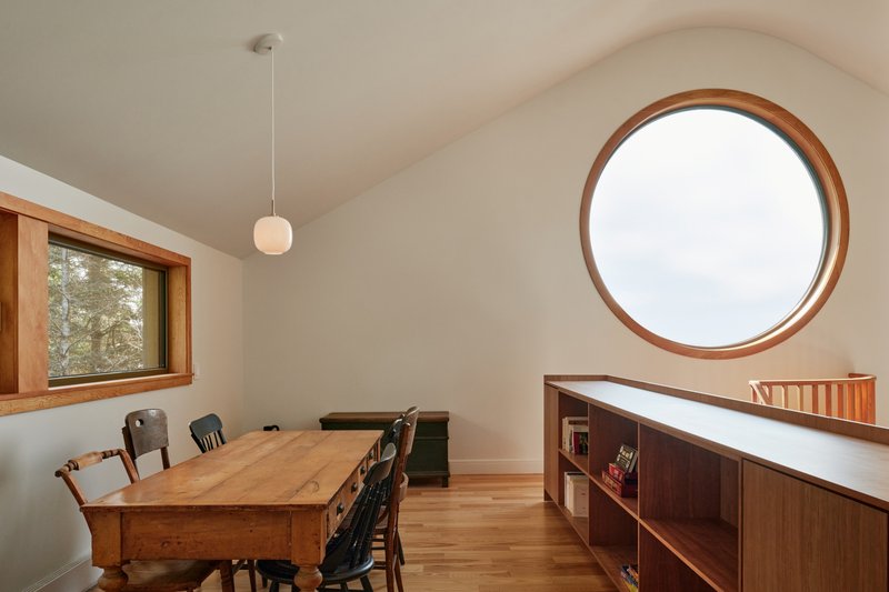 Upper floor study with circular window, low bookshelves and vaulted ceiling under soft daylight