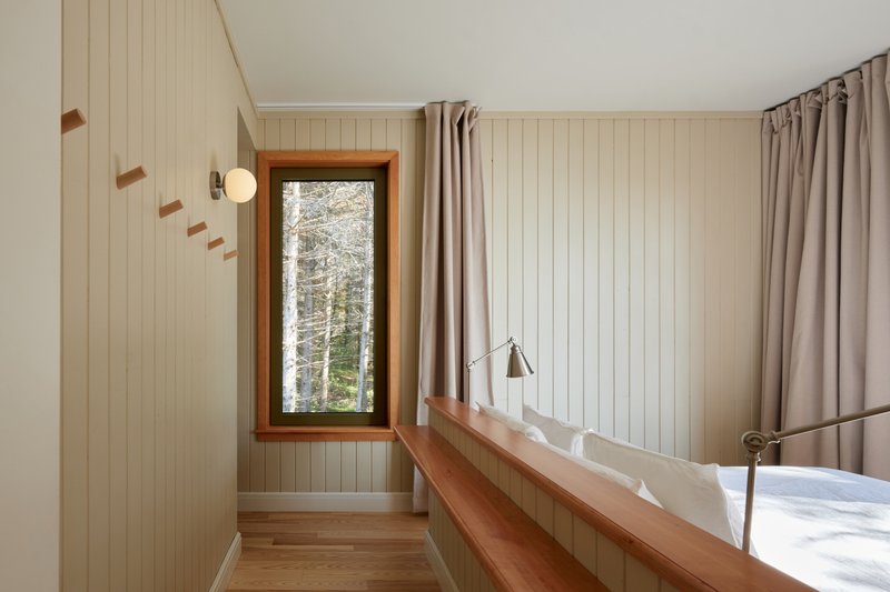 Bedroom with vertical tongue-and-groove paneling and a timber-framed window overlooking snowy trees