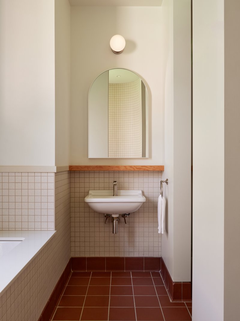 Bathroom corner with wall-hung sink beneath an arched mirror and sphere sconce