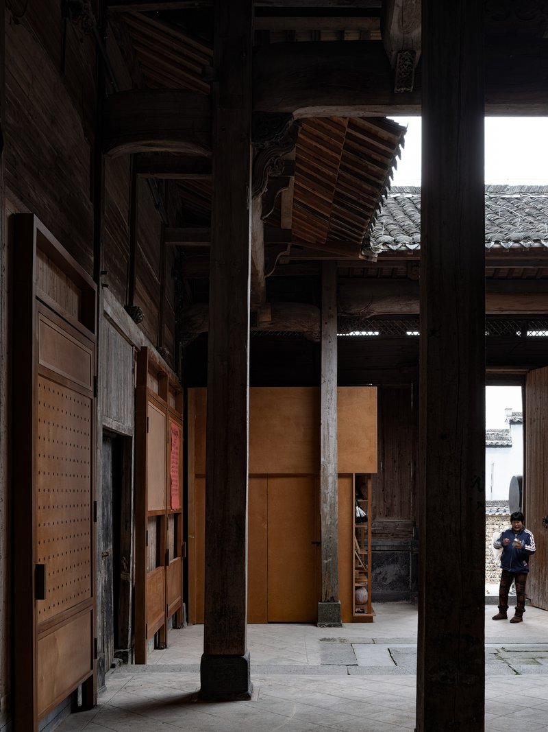 Interior passage with dark timber columns, carved brackets and a visitor standing in daylight