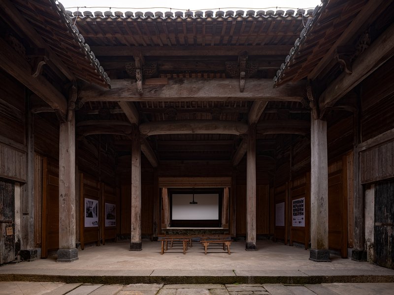 Central hall with timber post-and-beam structure, open skylight and projection screen flanked by wooden benches
