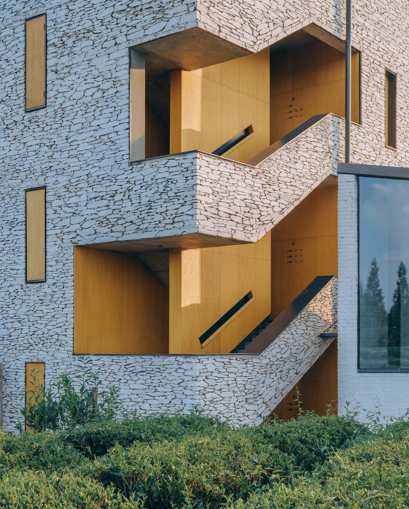 Stacked balconies with timber-lined recesses projecting from white terrazzo facade in afternoon sunlight